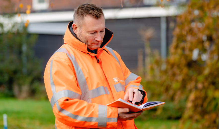 Medewerker in reflecterende veiligheidskleding registreert inspectiegegevens op een tablet tijdens een locatiecontrole.