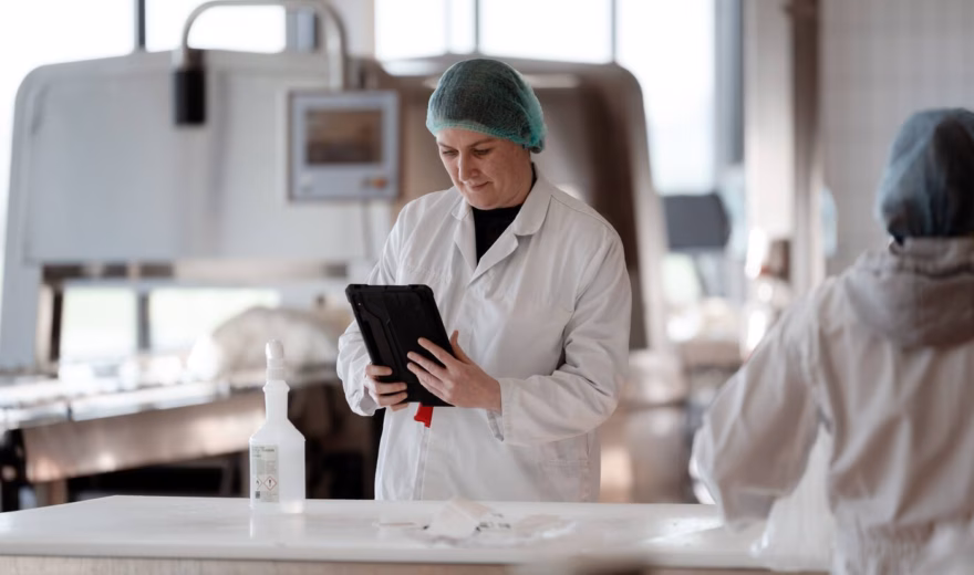 An employee in a production environment checks data on a tablet during a quality or process inspection.