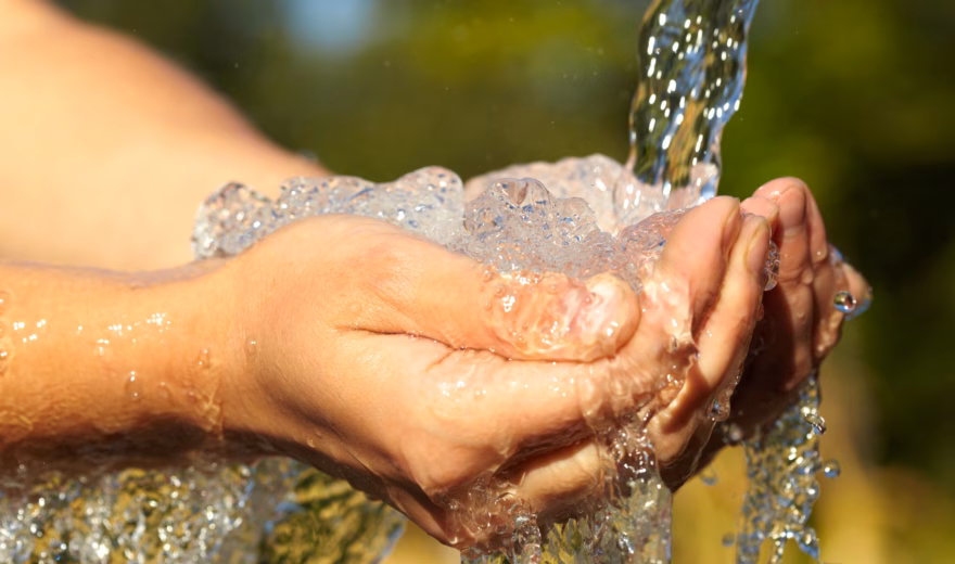 Mit den Händen unter fließendem Wasser aus einer natürlichen Wasserquelle aufgefangen.