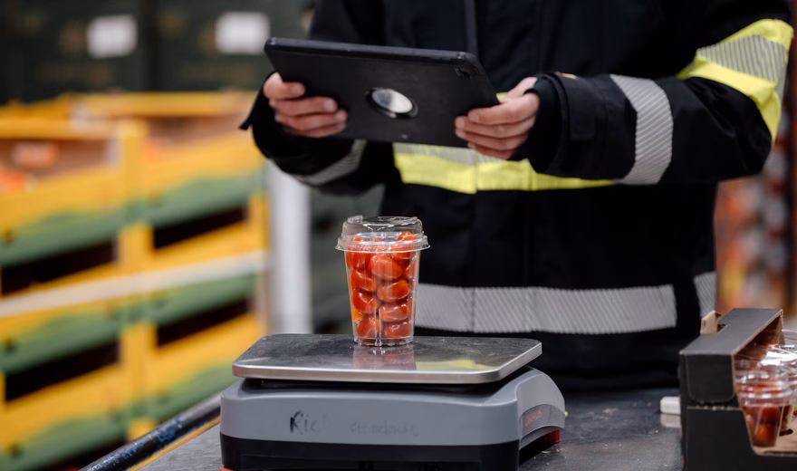 Ein Lagerarbeiter nutzt während einer logistischen Kontrolle ein Tablet neben einer Industriewaage mit verpackten Produkten.