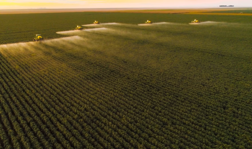 Mehrere Landmaschinen führen auf einer weitläufigen landwirtschaftlichen Fläche eine Pflanzenschutzbehandlung durch.