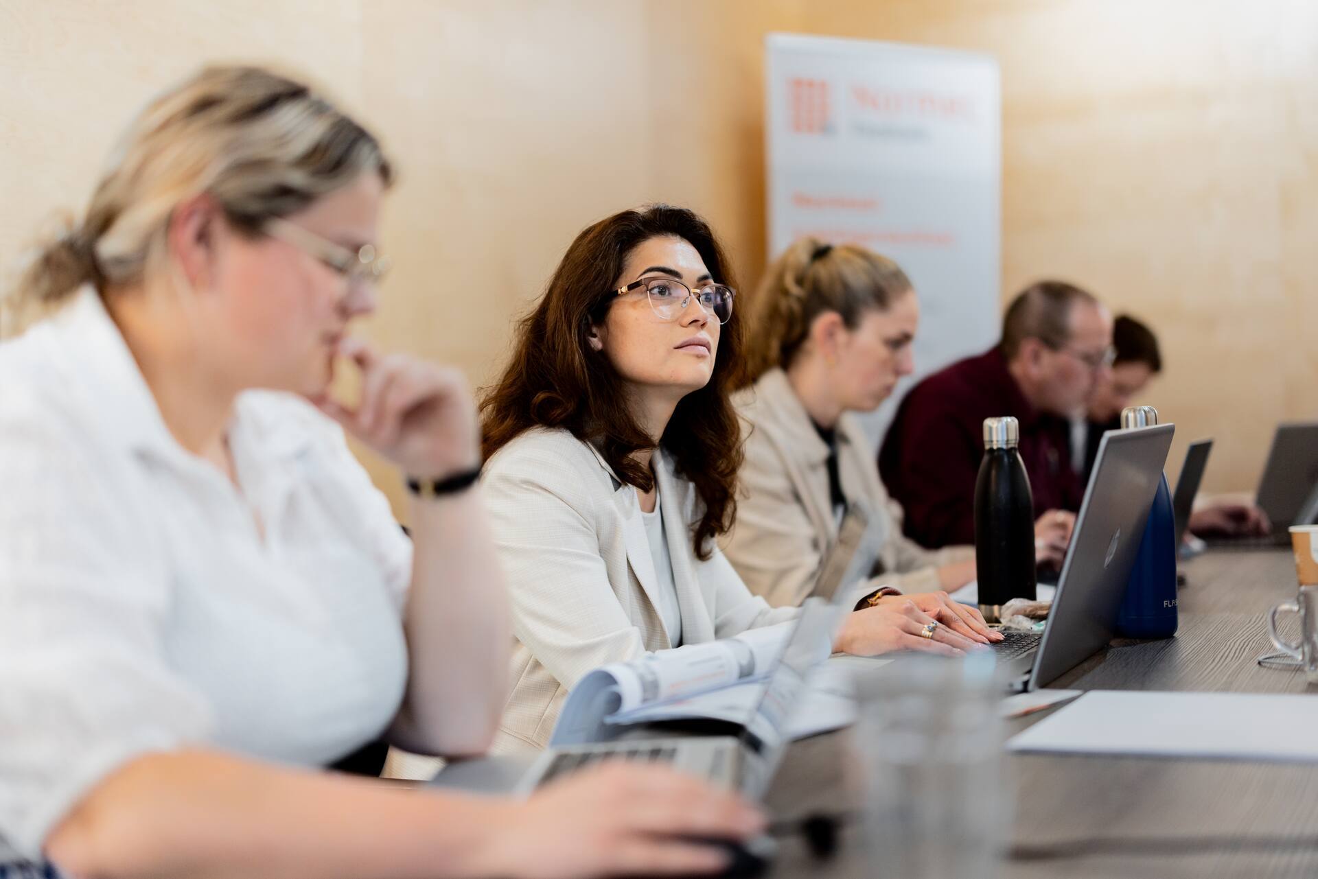 Deelnemers aan een zakelijke training of bijeenkomst werken met laptops aan een vergadertafel.