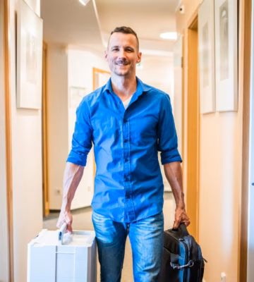 A person walks down a hallway carrying a briefcase and a bag for an on-site visit