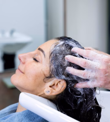 Eine Person erhält eine Haarwäsche im Friseursalon, während ihr Haar am Waschbecken mit Shampoo einmassiert wird.