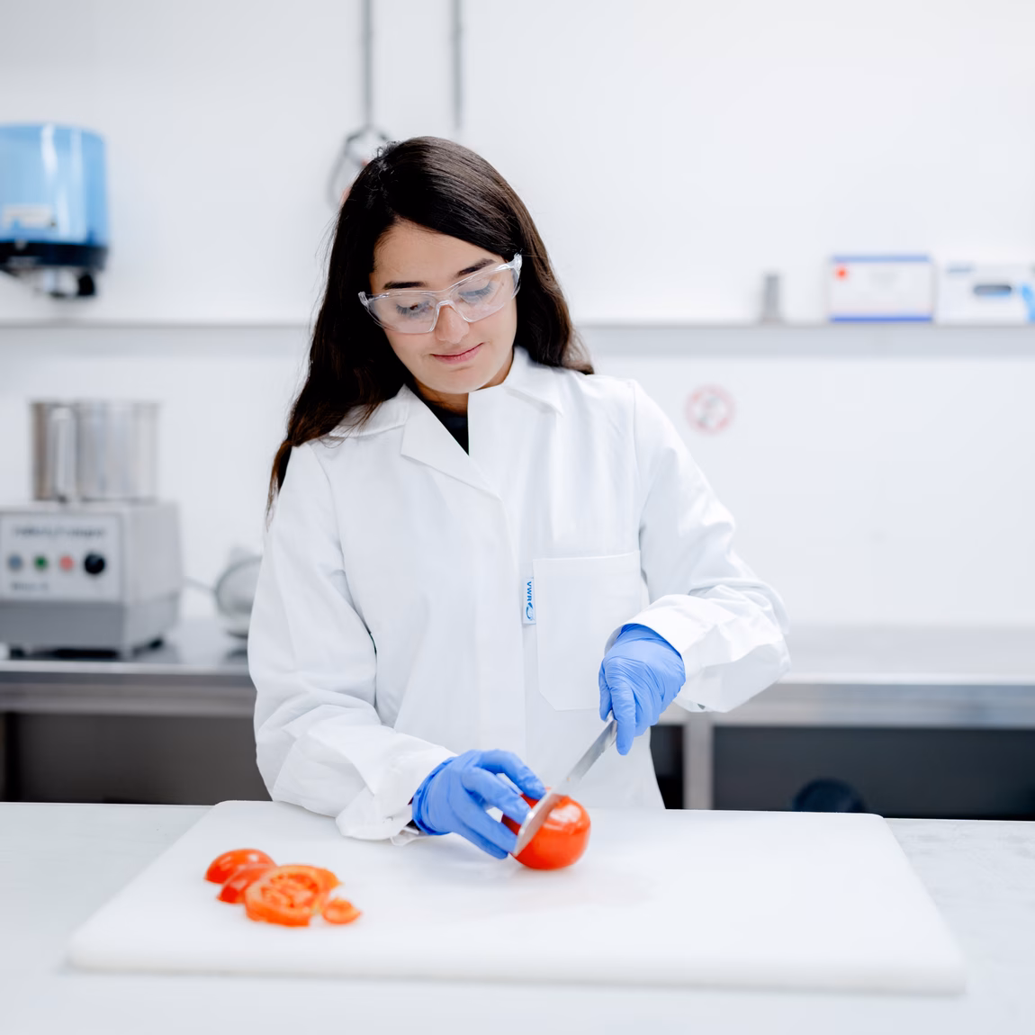 Laboratoriummedewerker onderzoekt een voedingsproduct op een werkbank in een laboratoriumomgeving. De afbeelding toont testen, kwaliteitscontrole en analyse ter ondersteuning van productveiligheid en compliance.