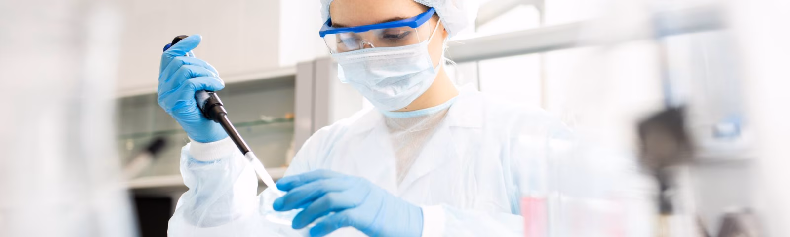 Ein Laborant in steriler Schutzkleidung führt während einer Laboranalyse einen Pipettiervorgang durch.