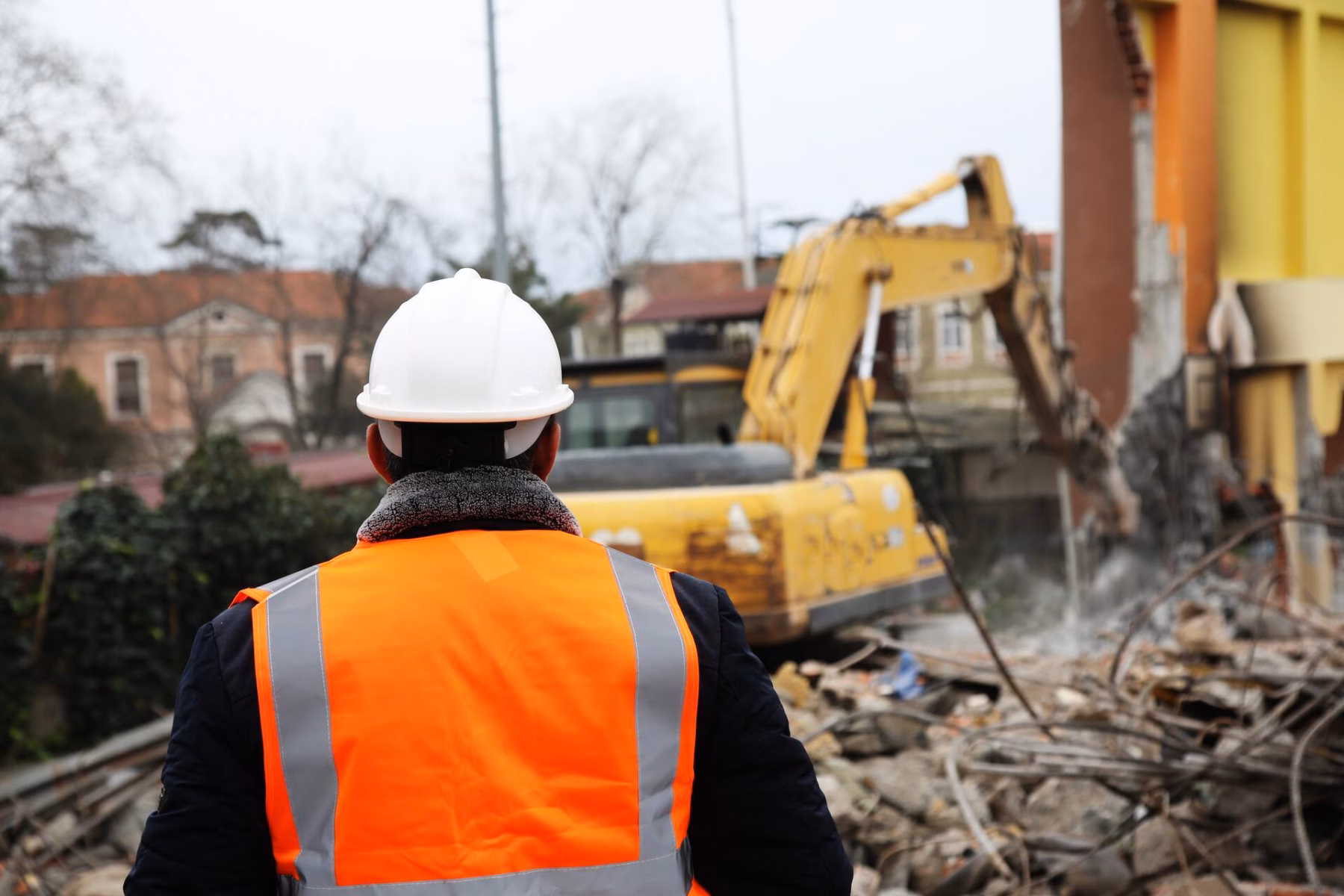 Ein Aufseher beobachtet Abbrucharbeiten mit einem Bagger auf einer Baustelle.