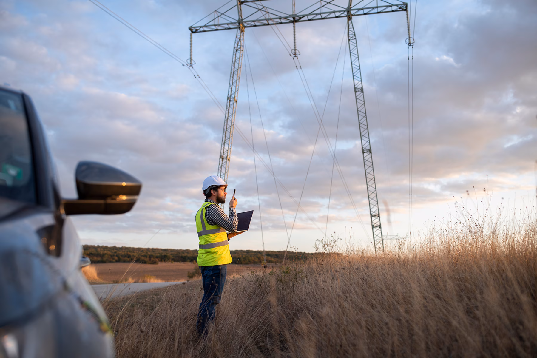 An employee is conducting inspection work near a high-voltage power pole in a rural area.