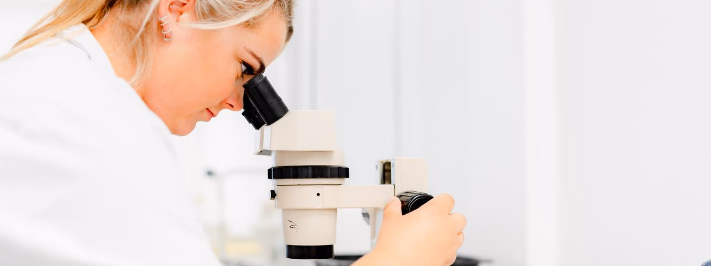 A woman is looking through a microscope at samples in a laboratory.