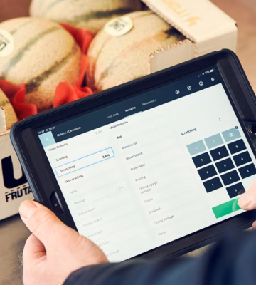 Ein Tablet mit Bestandsverwaltungssoftware wird bei der Kontrolle von Melonen in einer Lagerumgebung eingesetzt.