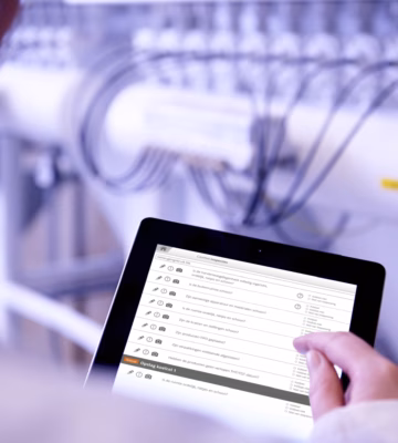 Persoon gebruikt een tablet om productie- of inspectiegegevens te controleren in een industriële omgeving met technische installaties.