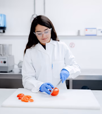 Ein Labormitarbeiter untersucht ein Lebensmittel auf einem Arbeitstisch in einer Laborumgebung. Das Bild zeigt Tests, Qualitätskontrolle und Analysen zur Gewährleistung der Produktsicherheit und der Einhaltung von Vorschriften.