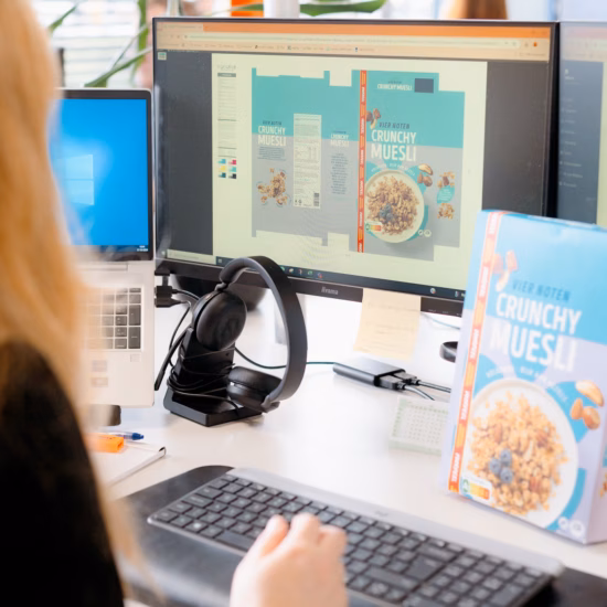 Ein Mitarbeiter arbeitet an einem Computerarbeitsplatz mit mehreren Monitoren an der Gestaltung einer Produktverpackung.