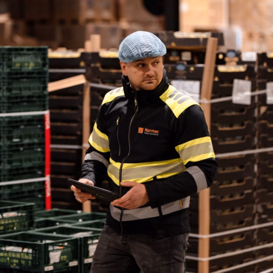 Magazijnmedewerker met tablet controleert logistieke processen tussen gestapelde kunststof kratten in een distributiecentrum.