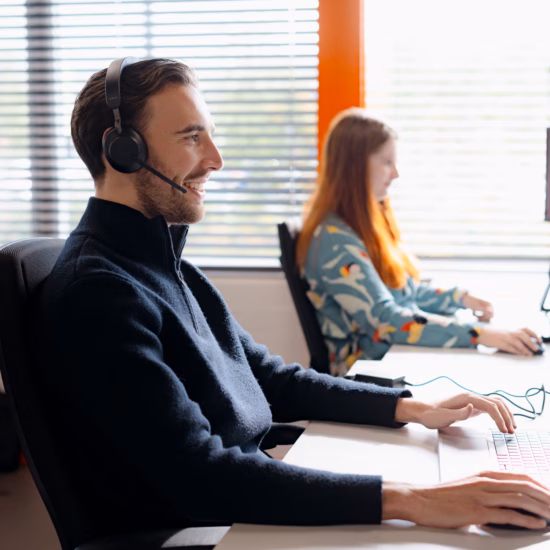 Mitarbeiter eines Kundendienstes arbeiten mit Headset und Computer an einem Büroarbeitsplatz.
