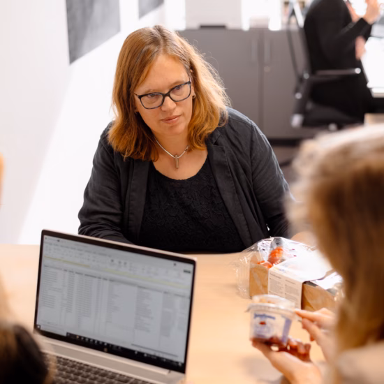 Besprechung am Besprechungstisch, bei der Mitarbeiter gemeinsam mit einem Laptop und Dokumenten arbeiten.