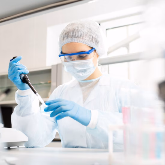 Laboratoriummedewerker in steriele beschermingskleding voert een pipetteerhandeling uit tijdens laboratoriumanalyse.
