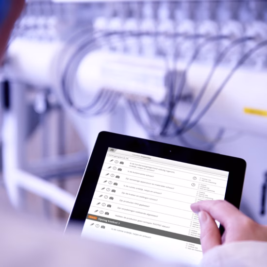 Eine Person nutzt ein Tablet, um Produktions- oder Inspektionsdaten in einer industriellen Umgebung mit technischen Anlagen zu überprüfen.
