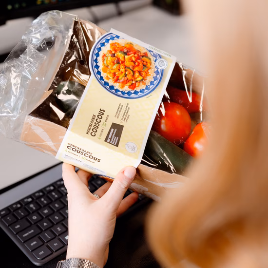 A person examines the packaging of a food product at a desk with a computer. The image illustrates product information, label verification, and quality assurance within food safety and compliance processes.