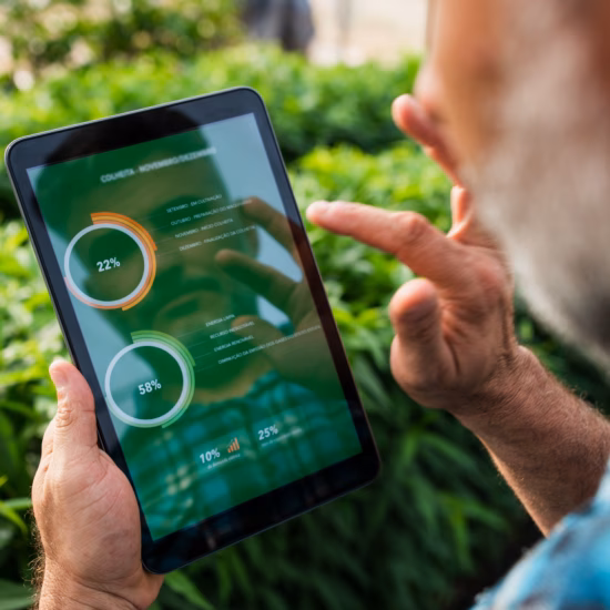 A man is in a green environment with bushes, looking at data on a tablet.