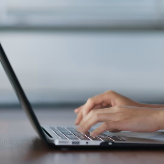 Hände, die auf einem Laptop an einem Schreibtisch in einer modernen Arbeitsumgebung tippen