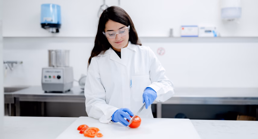 A laboratory technician wearing protective clothing performs a quality check on a tomato in a laboratory.