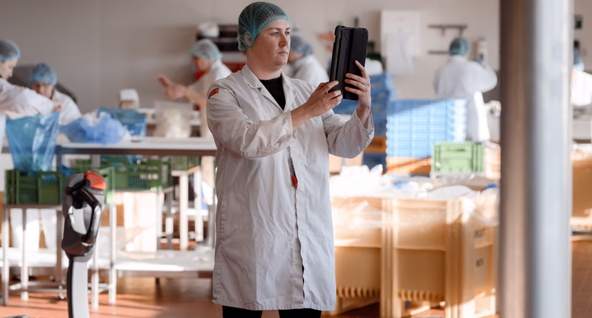 Un employé vêtu d'une blouse blanche de laboratoire inspecte des plateaux noirs dans un environnement de production dans le cadre d'un contrôle qualité.