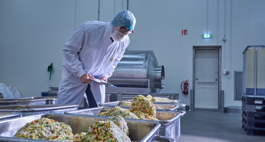Medewerker in hygiënekleding verwerkt voedingsproducten in een productieruimte voor voedselverwerking.