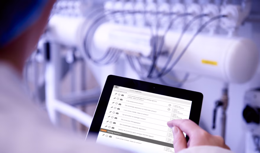 A person uses a tablet to check production or inspection data in an industrial setting with technical equipment.