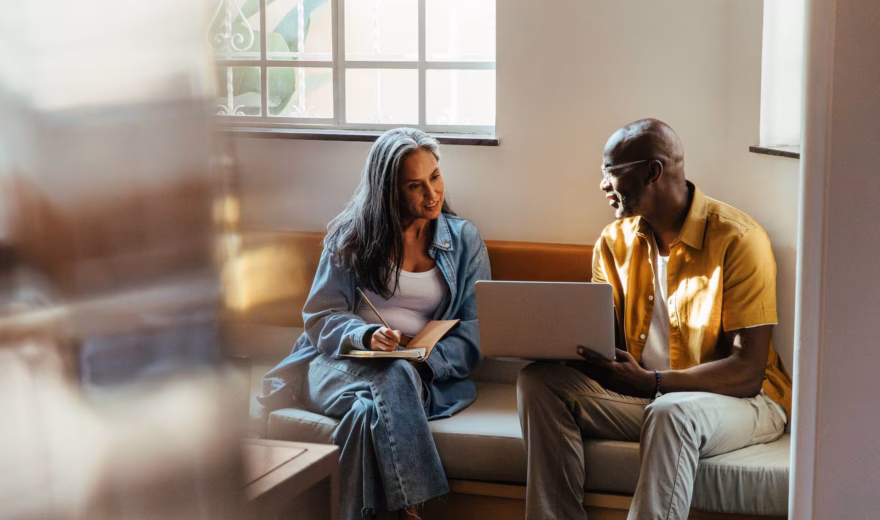 Manager and teammate collaborating on a project while sitting and discussing ideas with a laptop in a modern office environment.