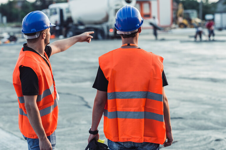 Mitarbeiter in Sicherheitskleidung und mit Bauhelmen auf einer Baustelle während der Arbeiten und der Arbeitskoordination