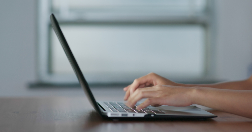 Hände, die auf einem Laptop an einem Schreibtisch in einer modernen Arbeitsumgebung tippen